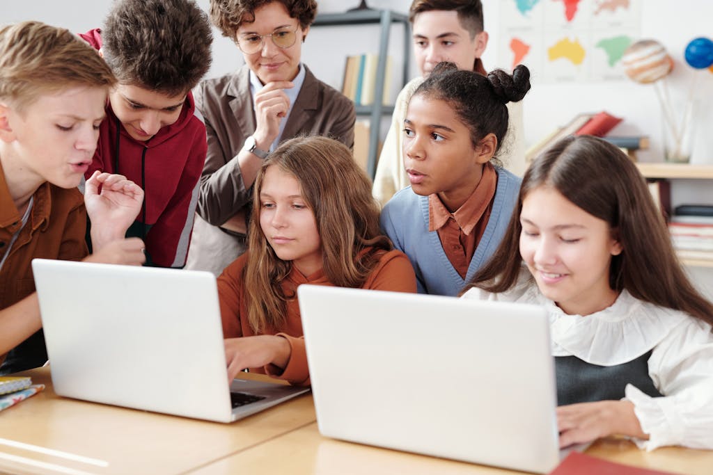 Teenage students actively collaborate on laptops in an educational environment with guidance from a teacher.