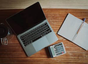 Top view of a desk with a laptop, calculator, and open notepad for work or study.